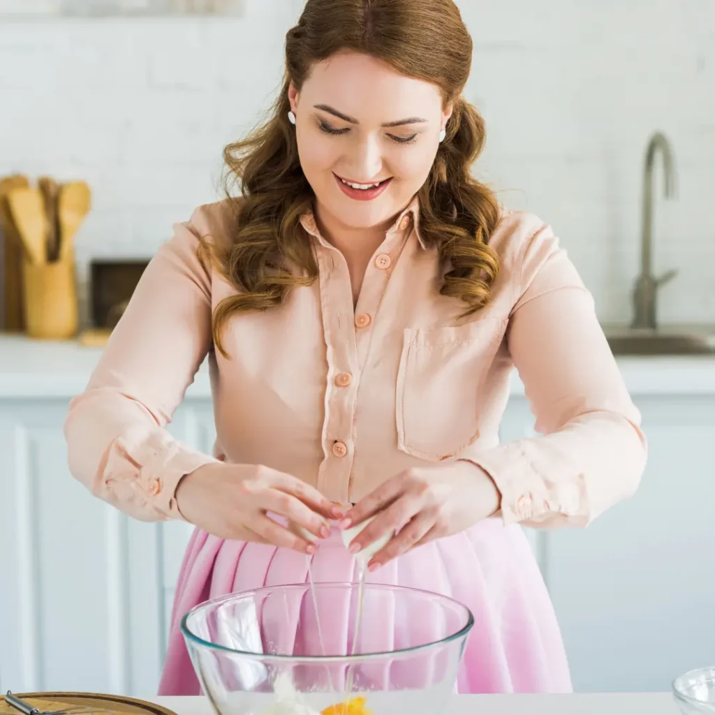 Young female pastry chef cracking an egg into a mixing bowl in a cozy kitchen.